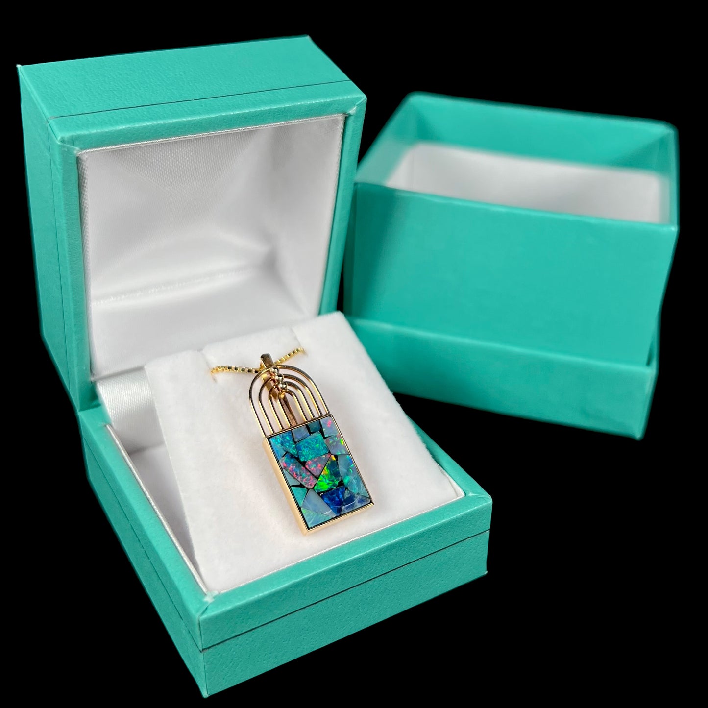 A gold mosaic opal necklace in a blue pendant box, with a bright green flash visible.