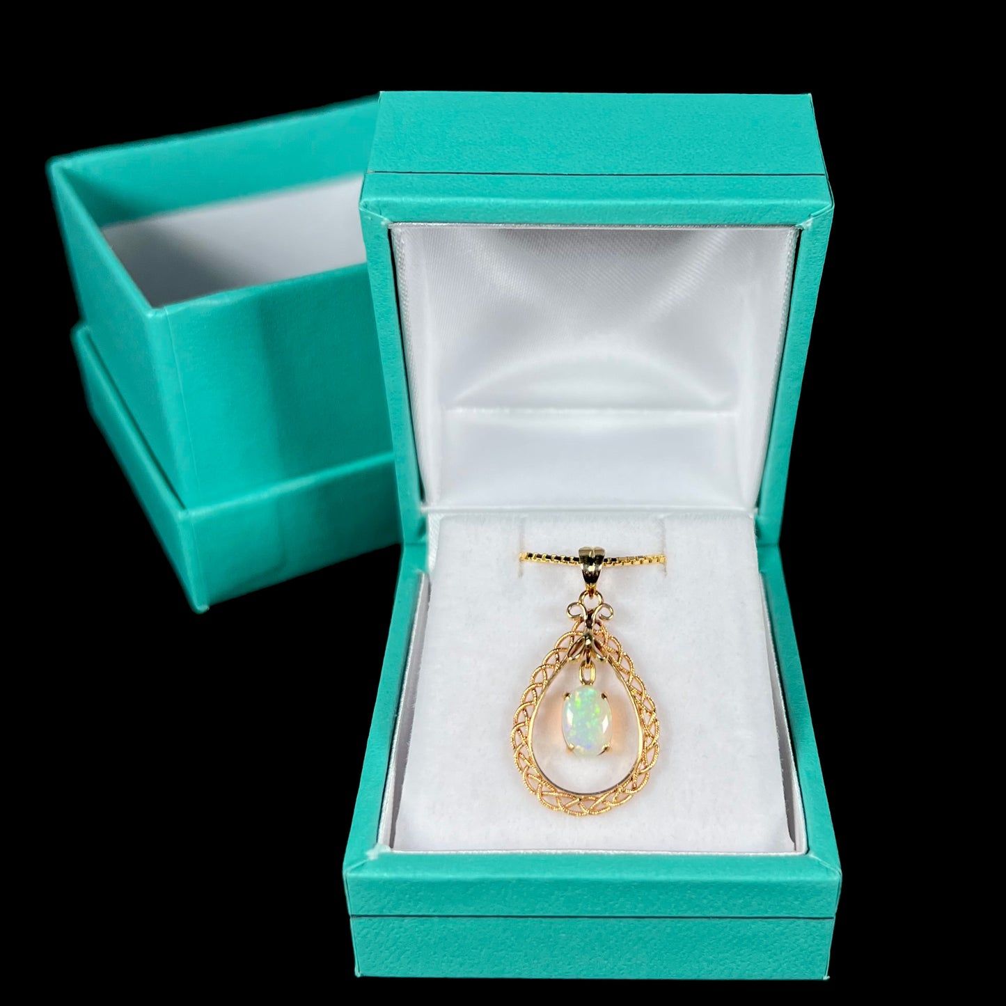 A gold opal filigree necklace displayed in a blue pendant box against a black background.