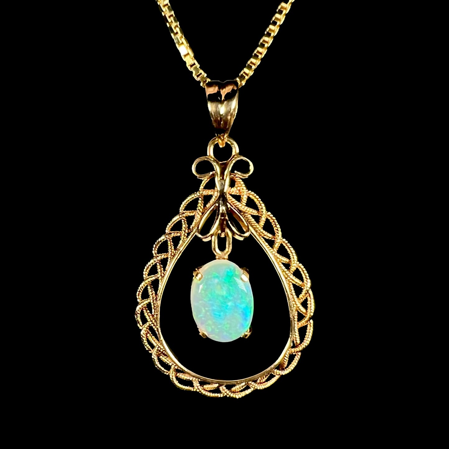 A macro close-up of an 18k gold opal filigree necklace against a black background, with a blue flash in the opal.