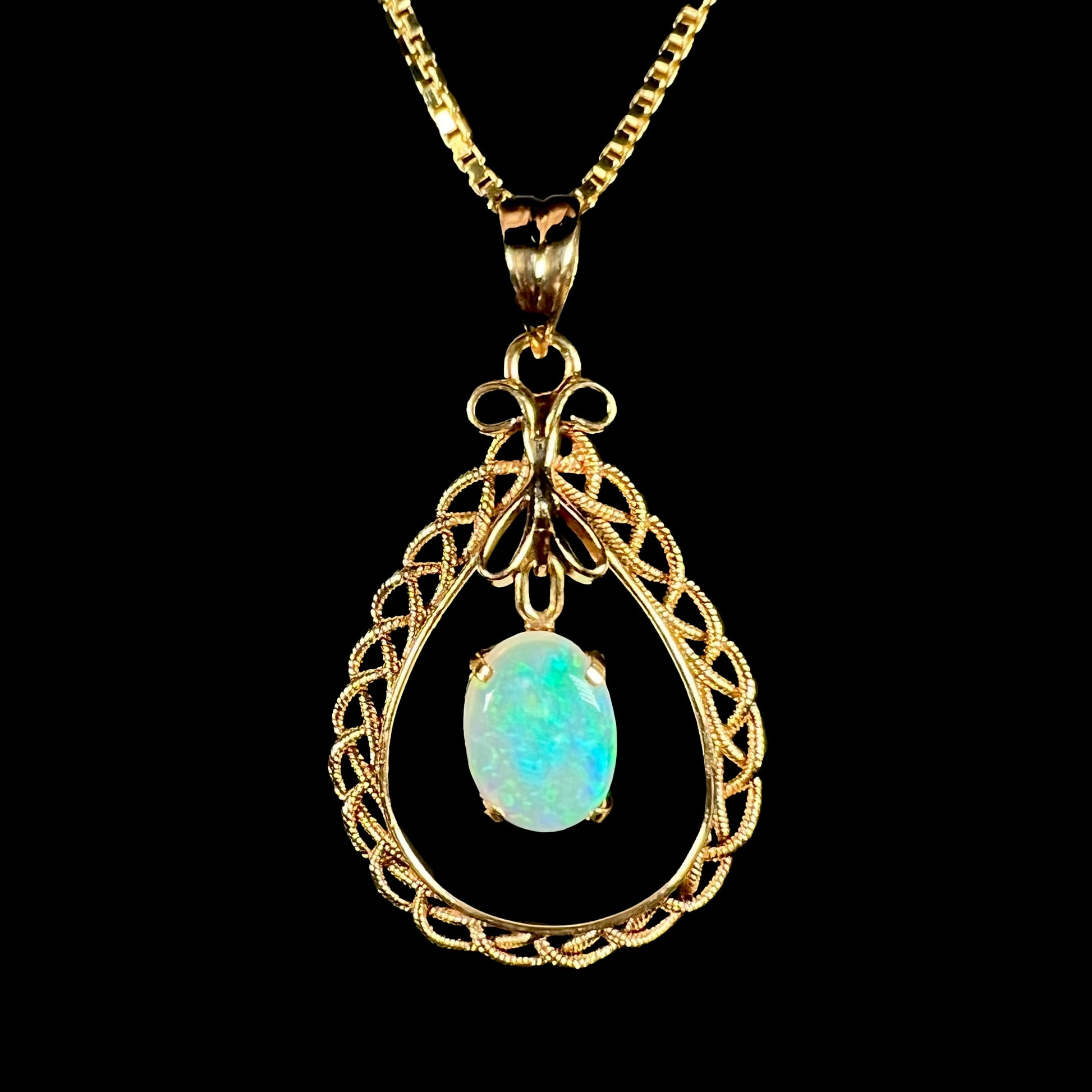 A macro close-up of an 18k gold opal filigree necklace against a black background, with a blue flash in the opal.