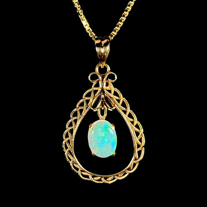 A macro close-up of an 18k gold opal filigree necklace against a black background, with a blue flash in the opal.