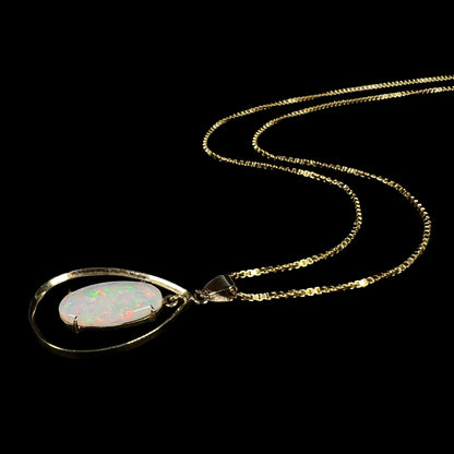 Angled stylistic shot of an 18k gold opal necklace lying against a black background, highlighting its minimalist frame.