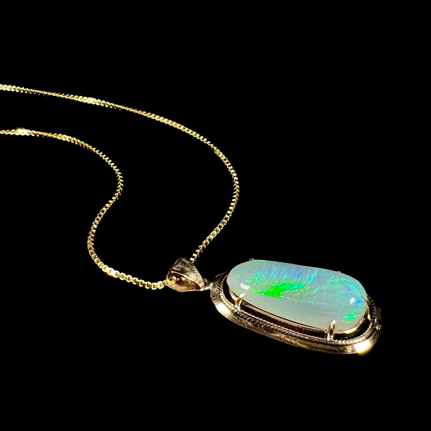 A stylish angled macro shot of an 18k gold Lightning Ridge opal necklace lying on a black background, revealing a bright green flash.