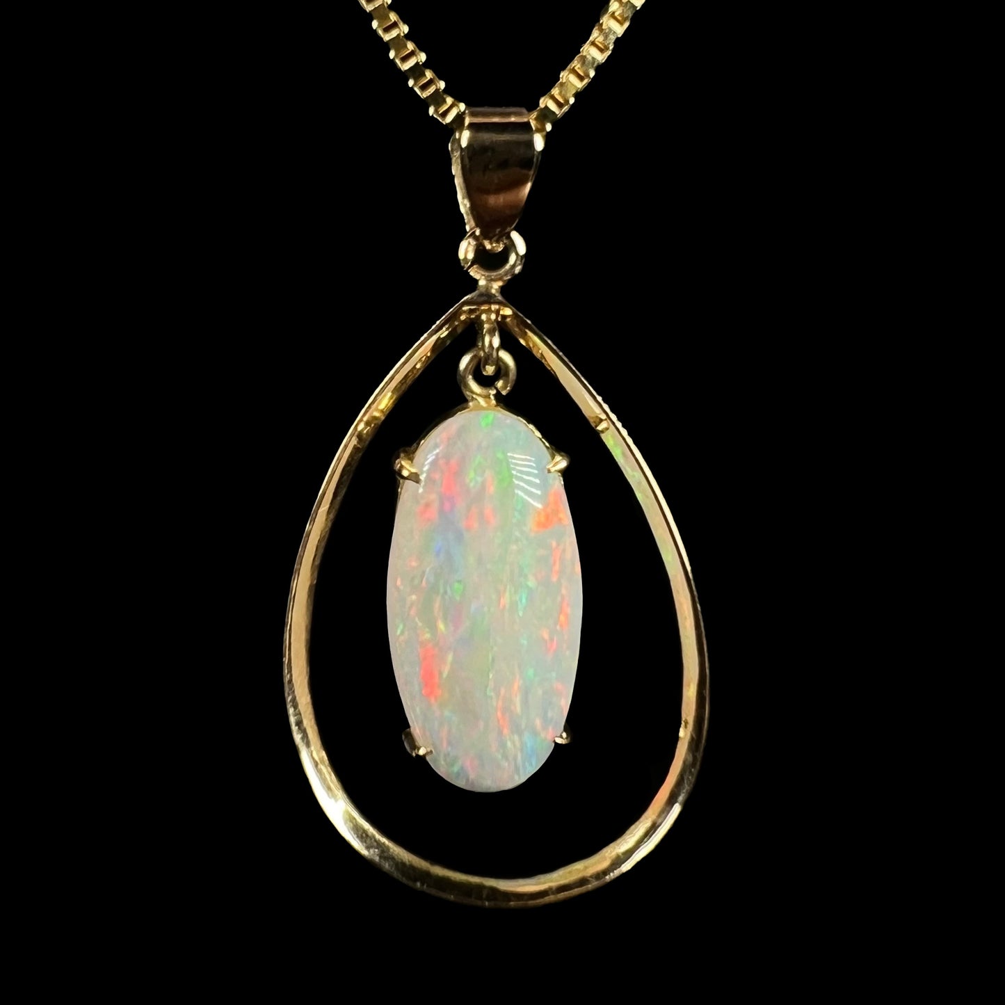 A delicate 18k gold opal pendant against a black background, featuring red flashes in the opal’s play-of-color.