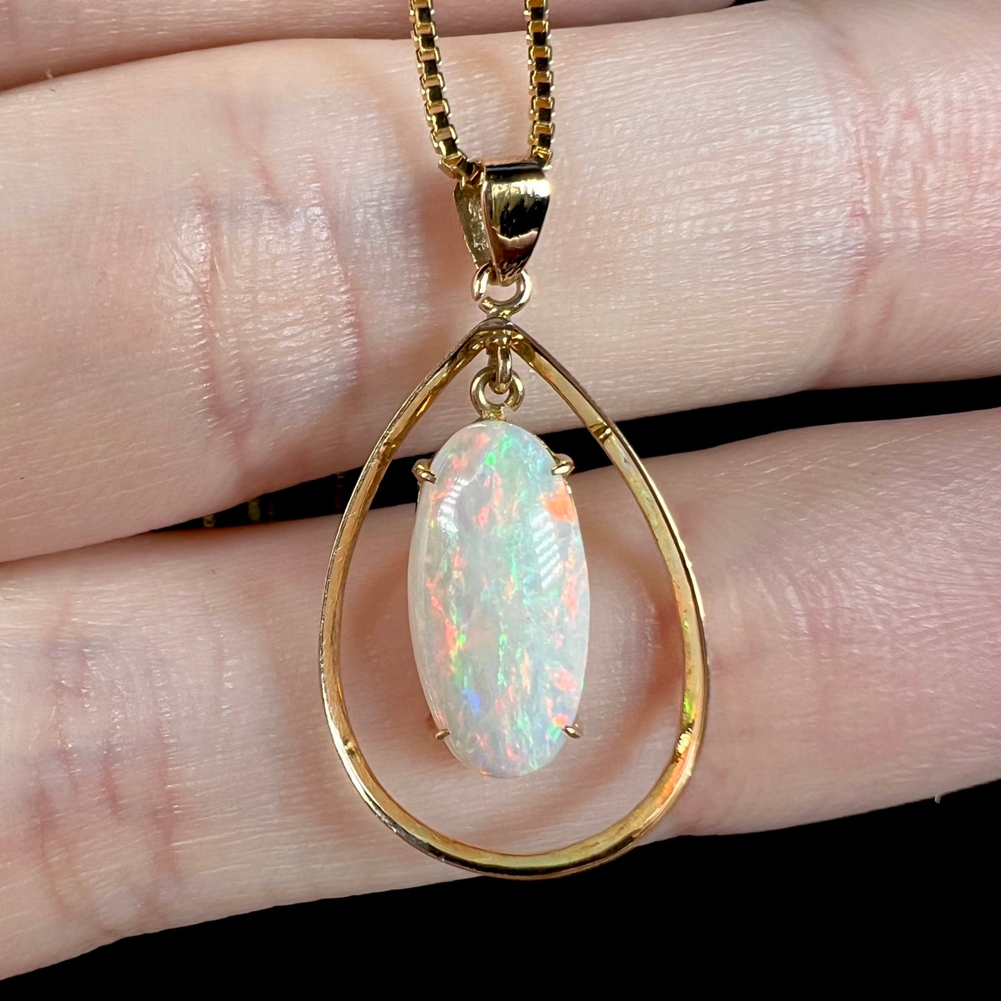 Macro view of an 18k gold opal necklace on fingers, revealing green and blue flashes in the opal’s fire.