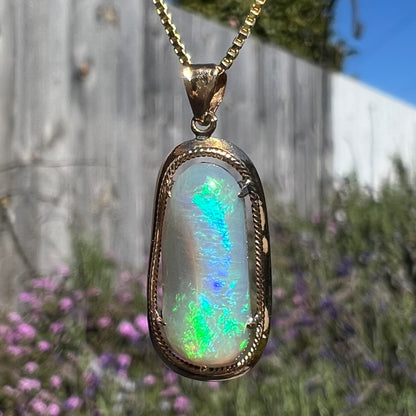 Macro close-up of an 18k gold opal necklace in sunlight, revealing vibrant green and blue flashes.