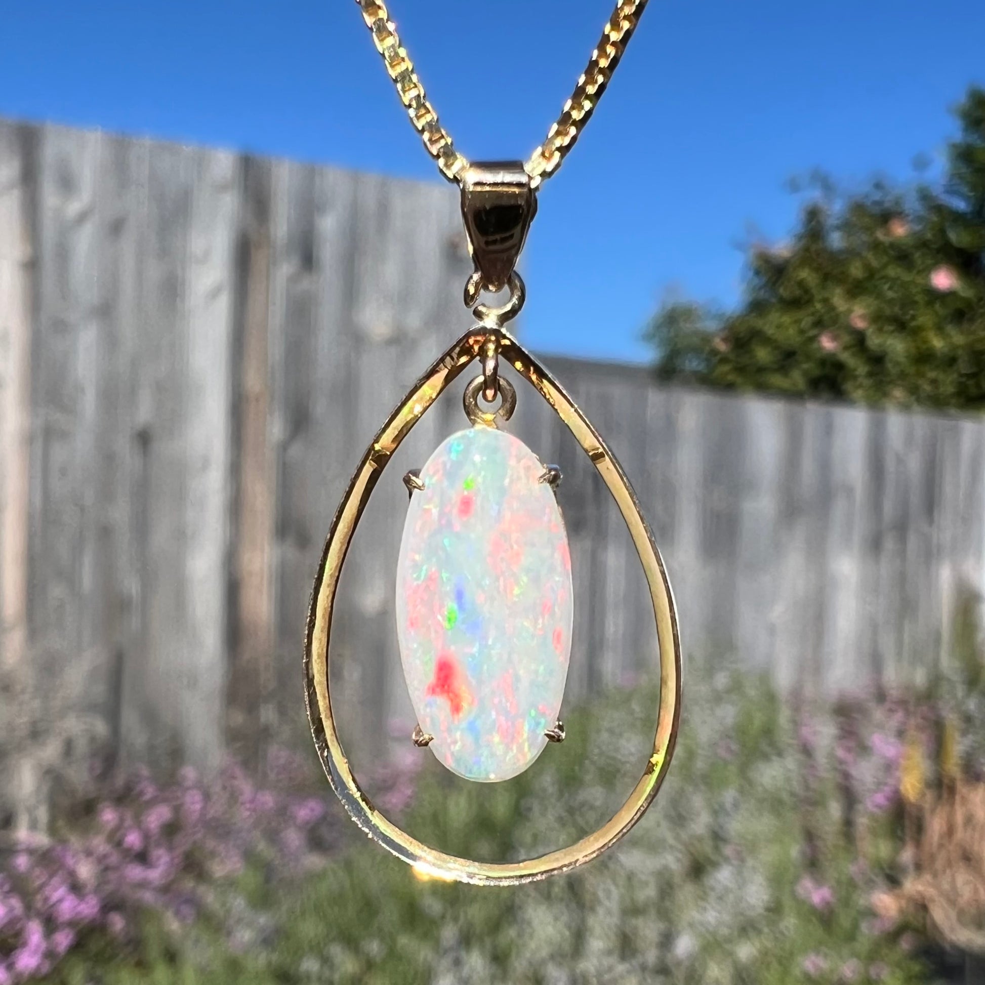 Macro close-up of an 18k gold opal necklace in natural light, revealing bright red flashes in the opal.