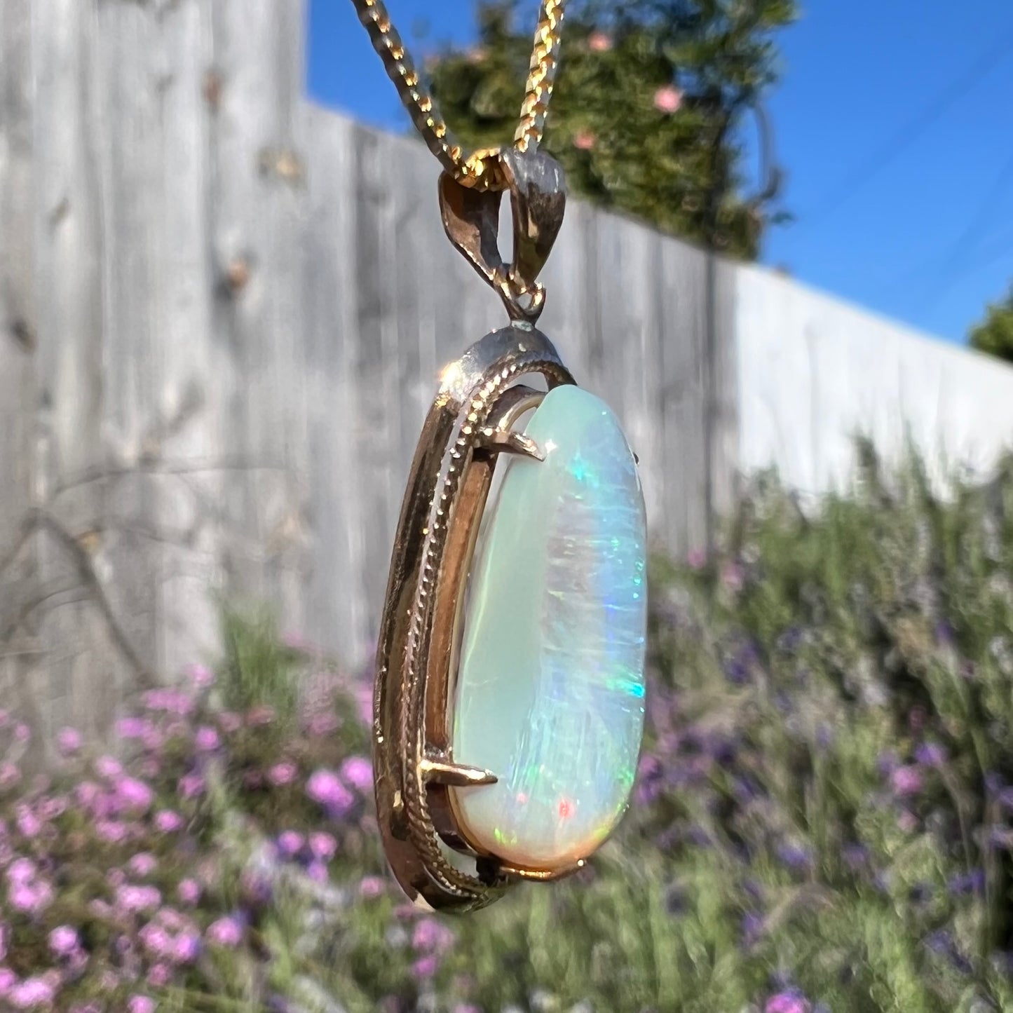 An 18k gold Lightning Ridge opal necklace, angled to show the opposite side, with minimal color play—faint blue and a small red flash visible.