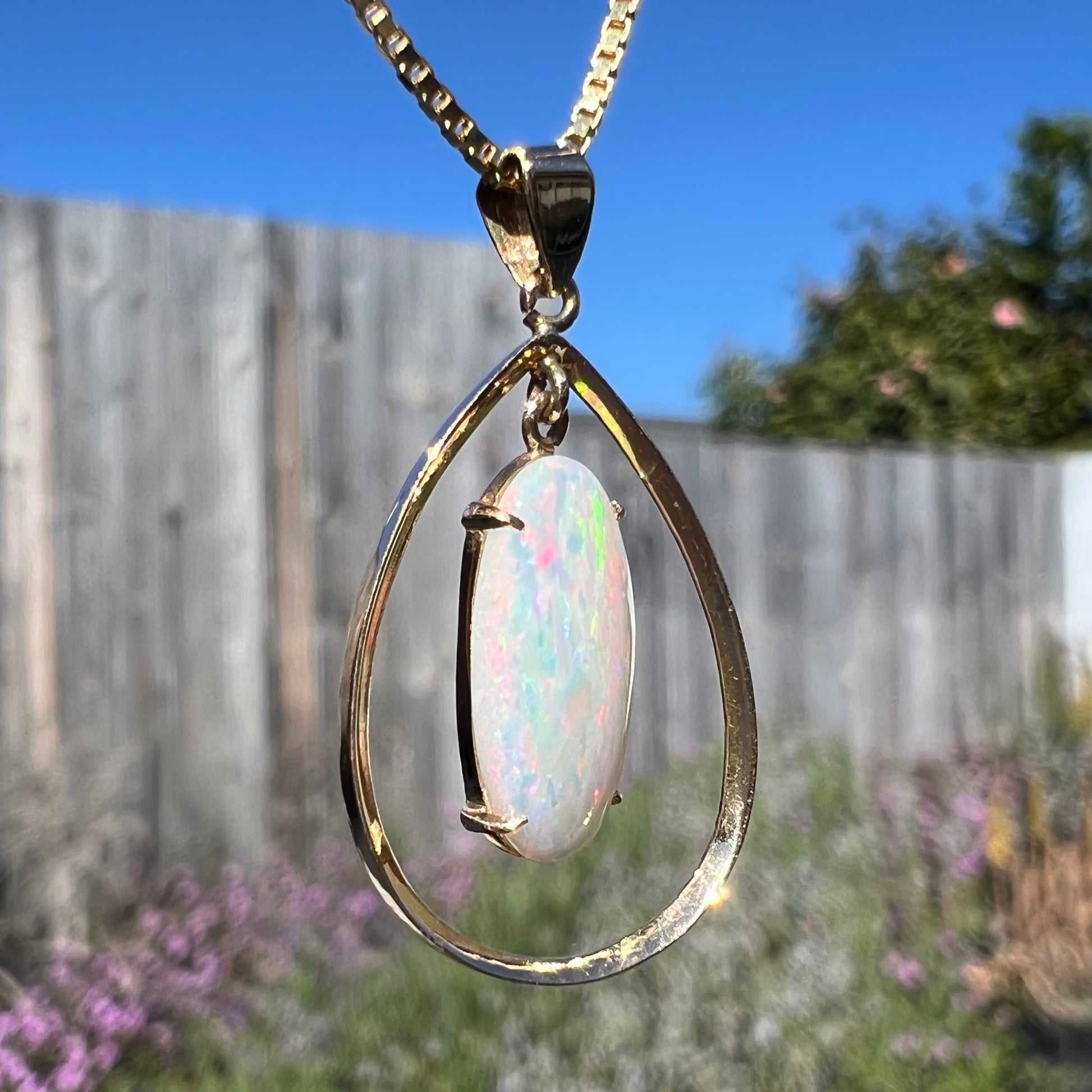 Macro shot of an 18k gold opal necklace outdoors, twisted at an angle to reveal subtle red and blue flashes with a green-striped flash.