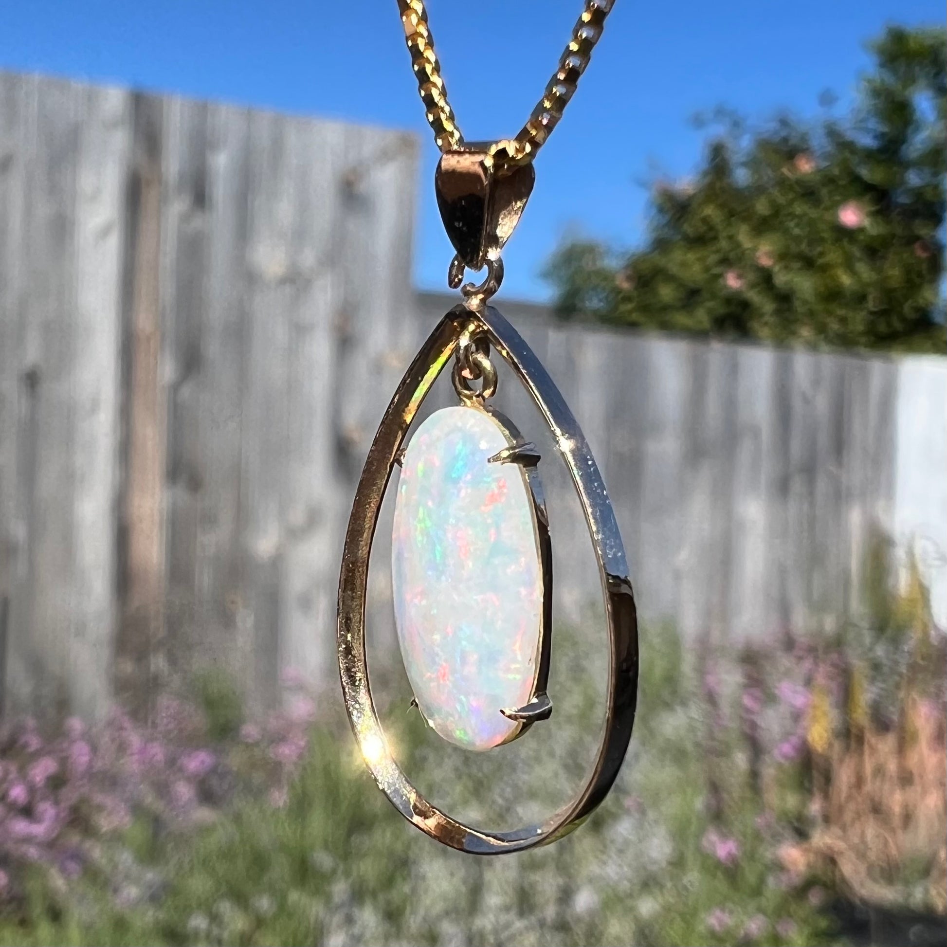 Angled outdoor shot of an 18k gold opal necklace, displaying subtle red and blue flashes in the opal under sunlight.