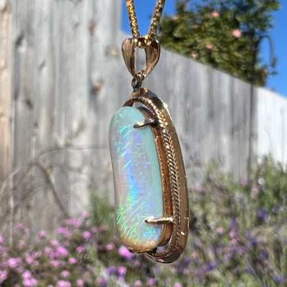 An 18k gold Lightning Ridge opal necklace, angled further to show more of a side view, with faint green and blue streaks visible.