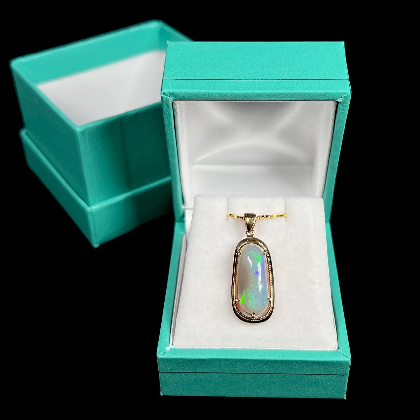 A refined 18k gold opal necklace displayed in a blue pendant box against a black background.