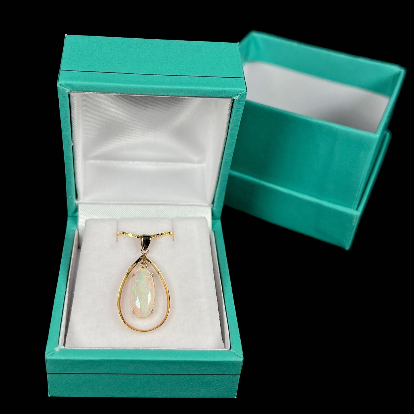 A refined 18k gold opal necklace displayed in a blue pendant box against a black background.