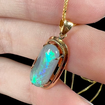 Side view of an 18k gold Lightning Ridge opal necklace, with bright blue and teal flashes along its surface.