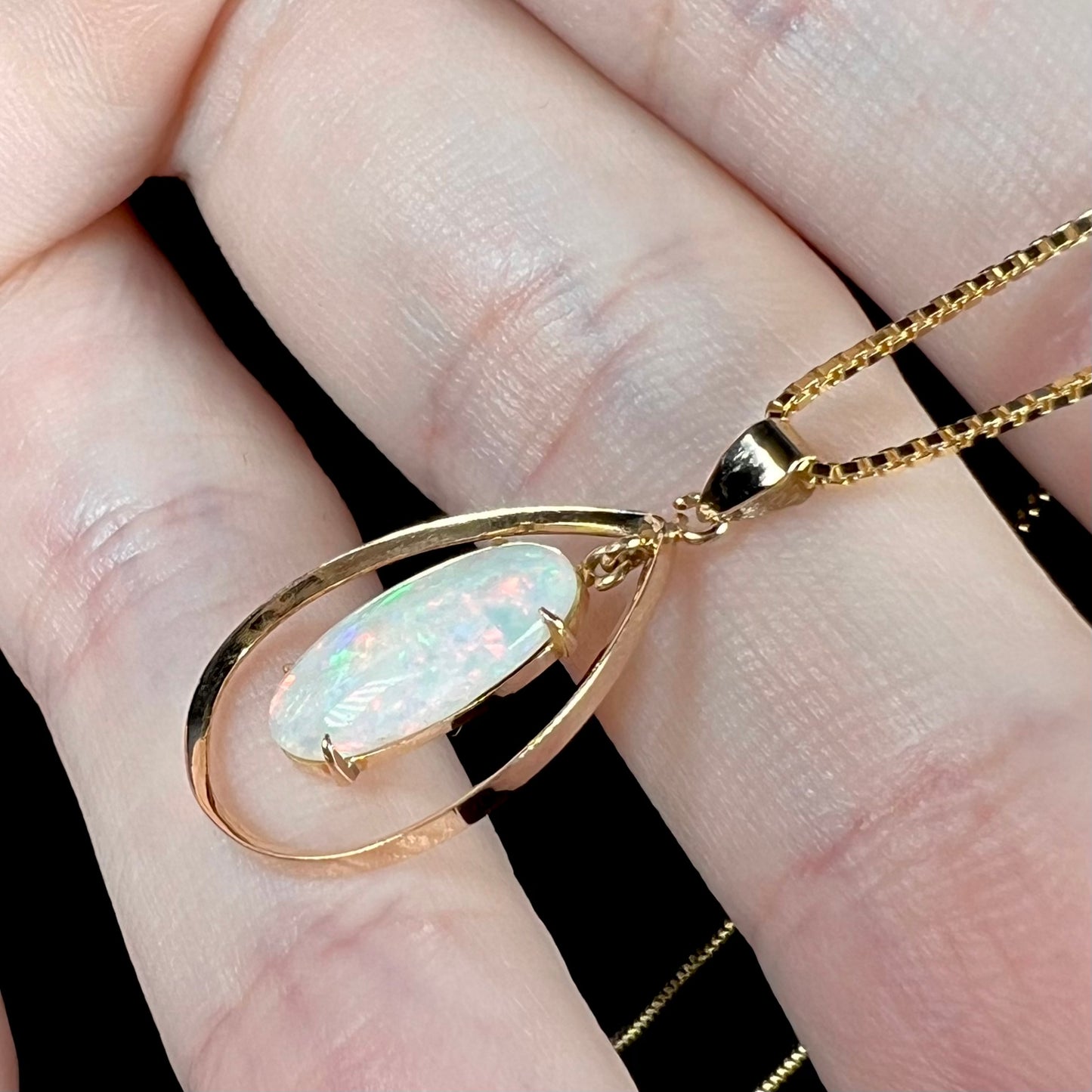 Side-angle of an 18k gold opal necklace, featuring soft pinkish-orange flashes in the opal.