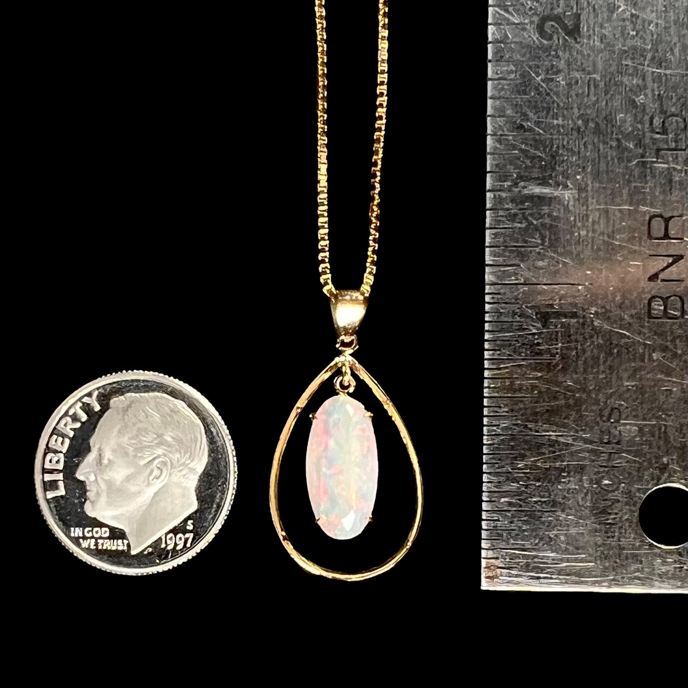 An 18k gold opal necklace next to a dime and ruler for scale, measuring approximately 1 inch long.