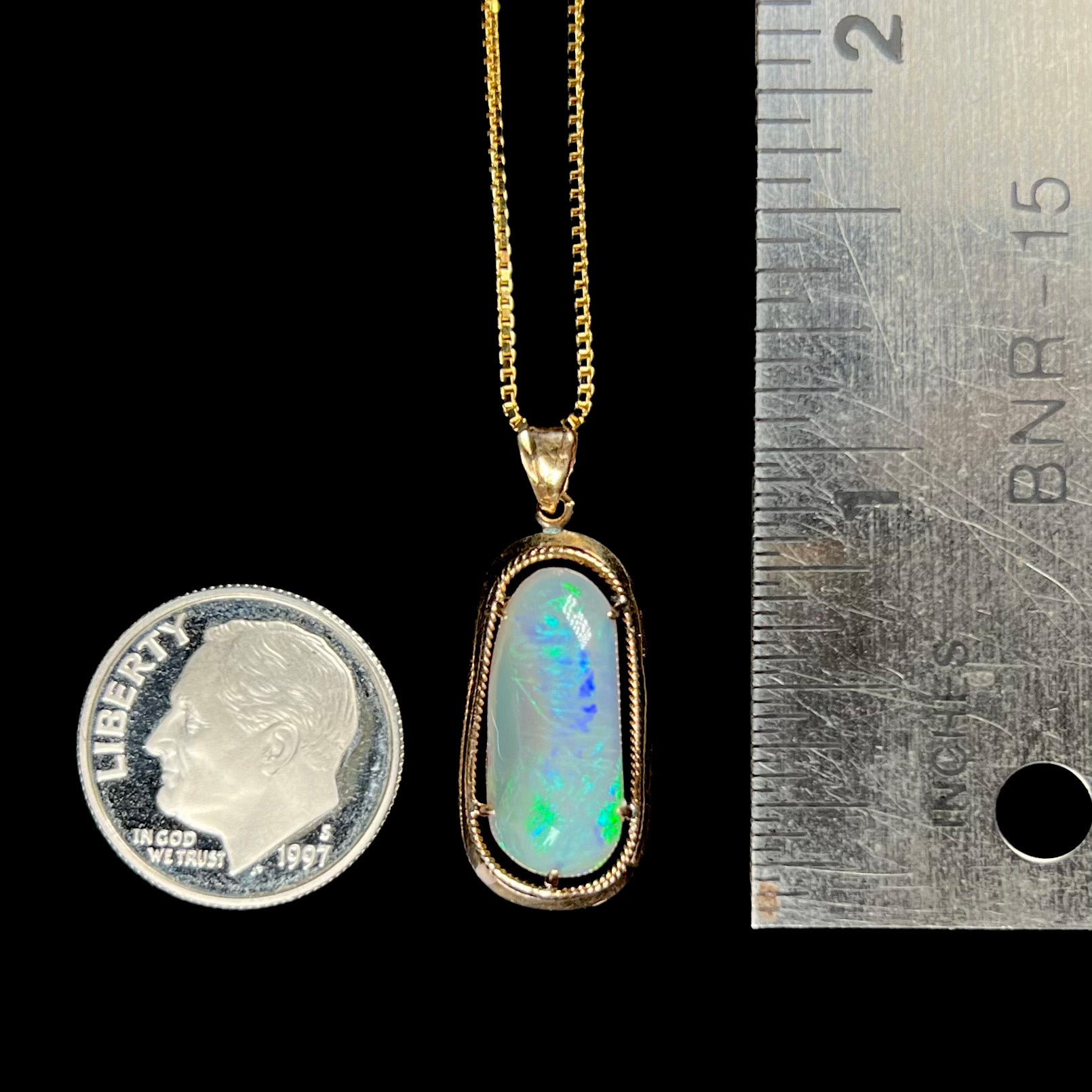 An 18k gold opal necklace next to a dime and ruler for scale, measuring approximately 1 inch long.