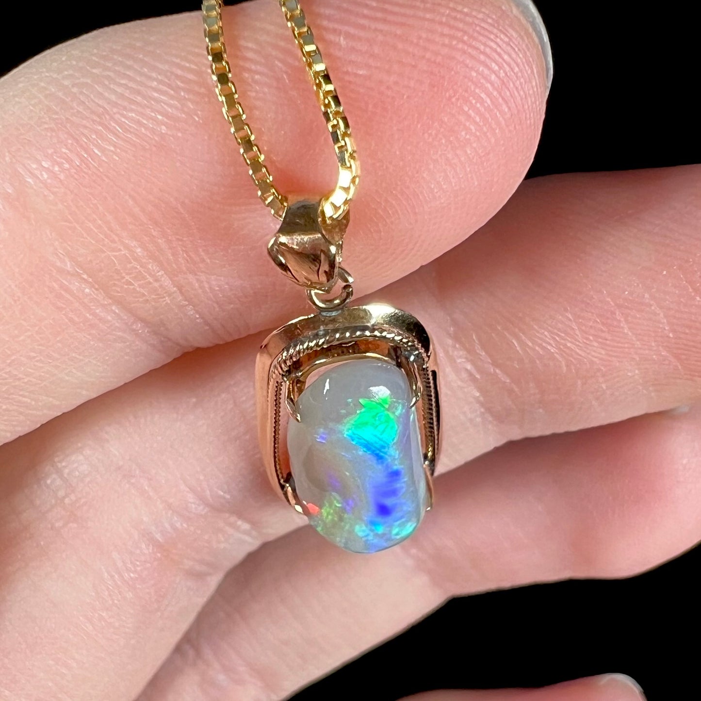 Top-down macro shot of an 18k gold Lightning Ridge opal necklace, showcasing an explosion of vivid blue and green colors.