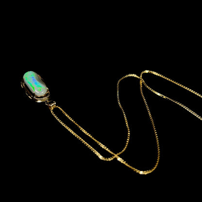 An 18k gold Lightning Ridge opal necklace captured from a top-down angle, showing vibrant blue and green flashes along its ridge.