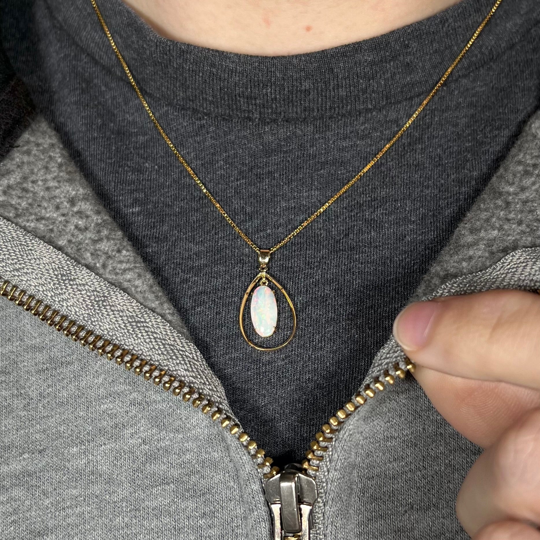 An 18k gold opal necklace worn on a black t-shirt with a partially zipped sweatshirt.