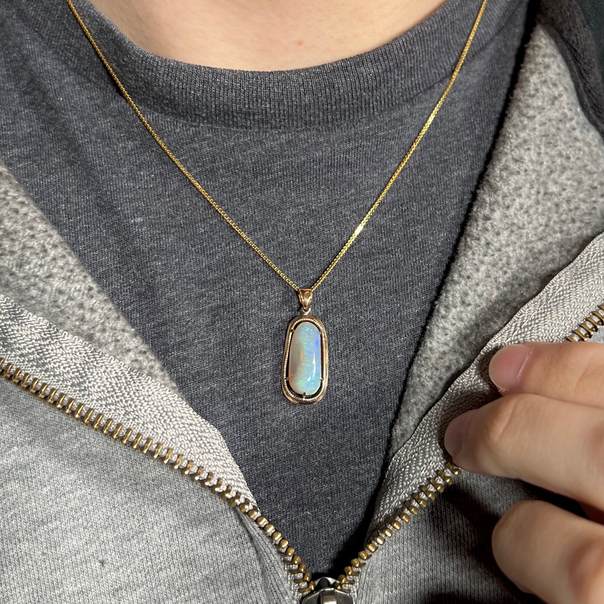 An 18k gold opal necklace worn on a black t-shirt with a partially zipped sweatshirt, showing no visible color play.