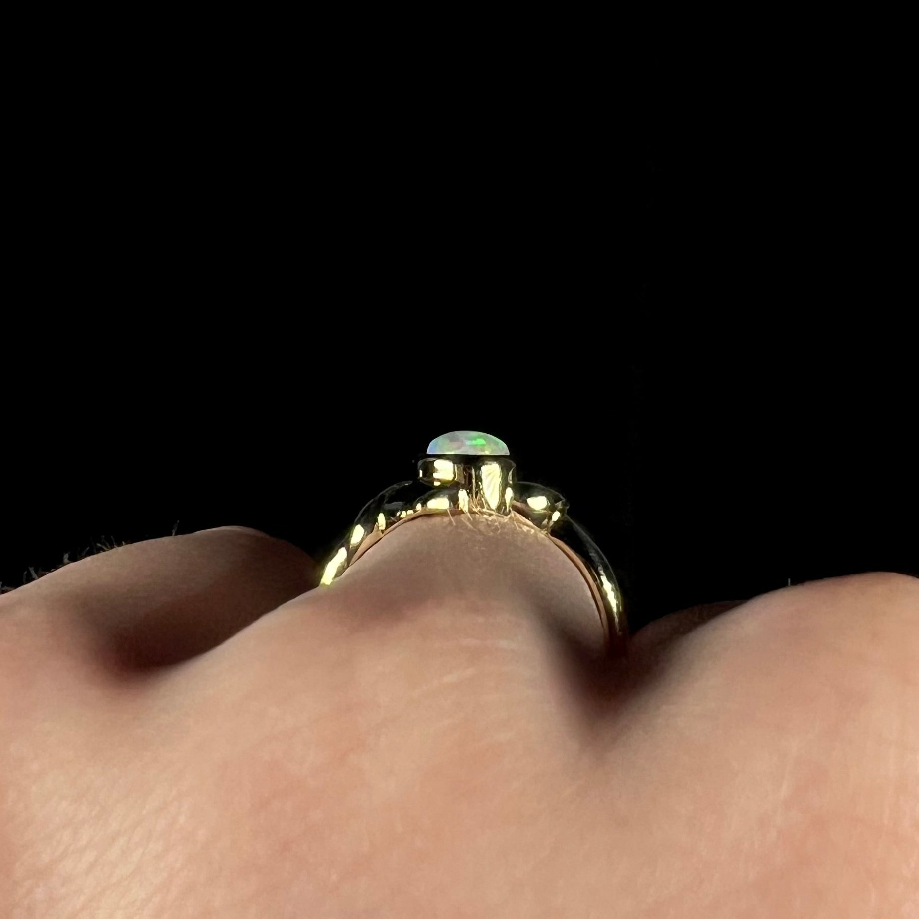 The gallery view of an 18 karat gold opal ring, worn on a finger.