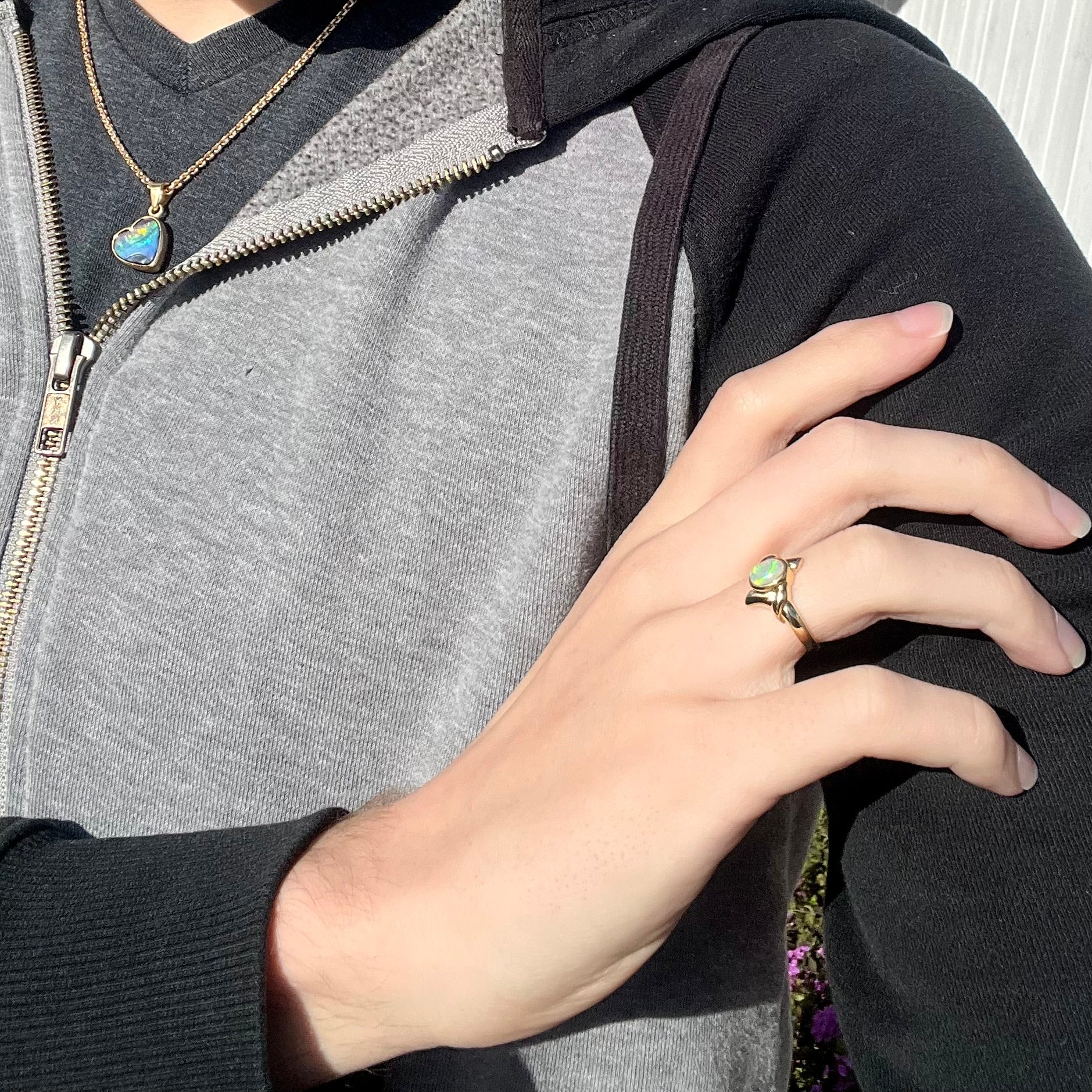 An 18k gold crystal opal engagement ring worn on a model's hand in the sunlight.