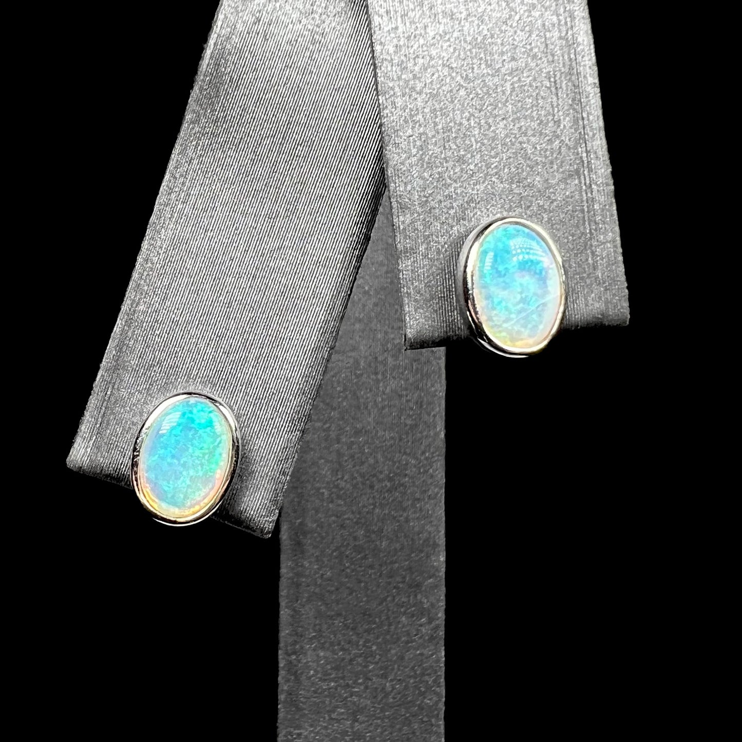 Pair of 18k white gold Australian crystal opal stud earrings with gentle blue green play of color on earring display from front close-up view.