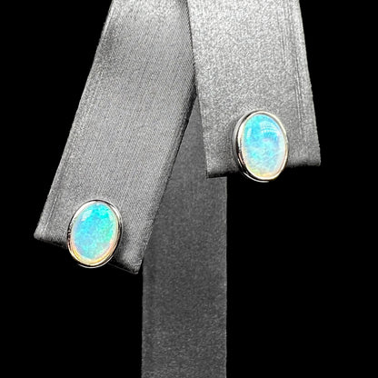 Pair of 18k white gold Australian crystal opal stud earrings with gentle blue green play of color on earring display from front close-up view.