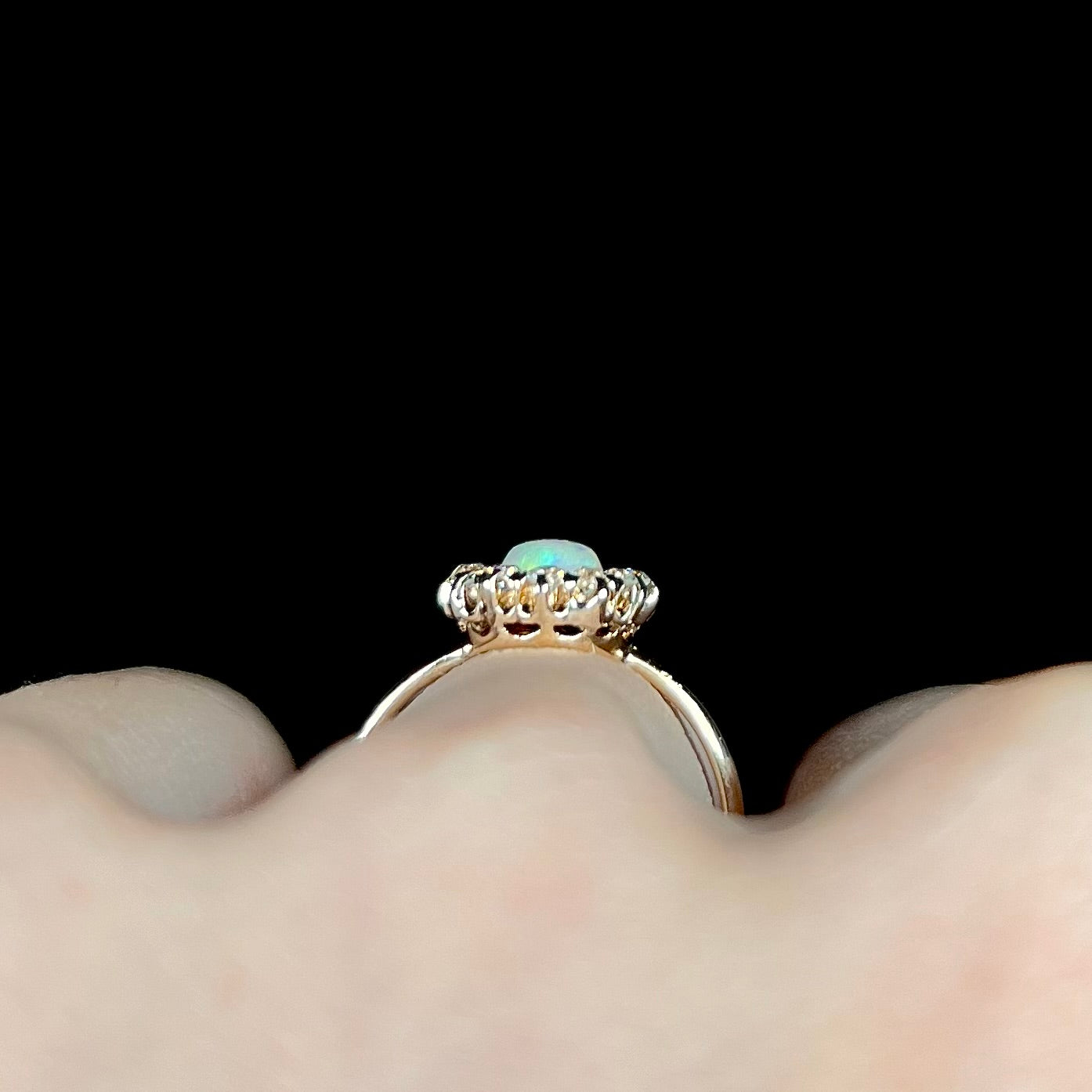 The gallery of an Edwardian era opal and diamond halo engagement ring on a hand.  The ring is yellow gold.