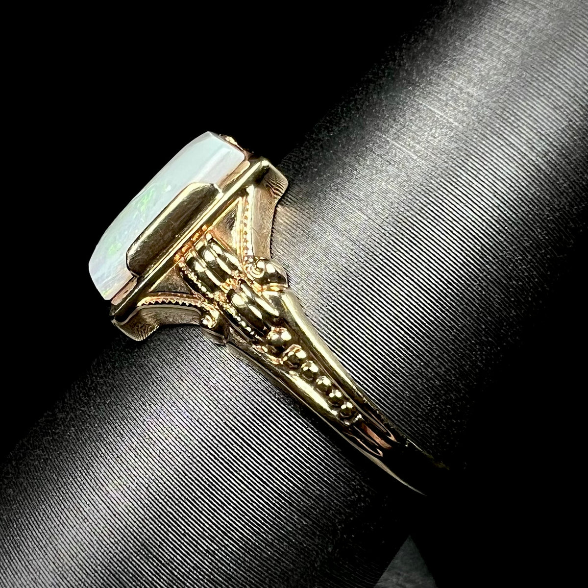 Side view of a c.1920s era gold opal ring on a ring display, the ring's ornate Art Deco-style shank in focus
