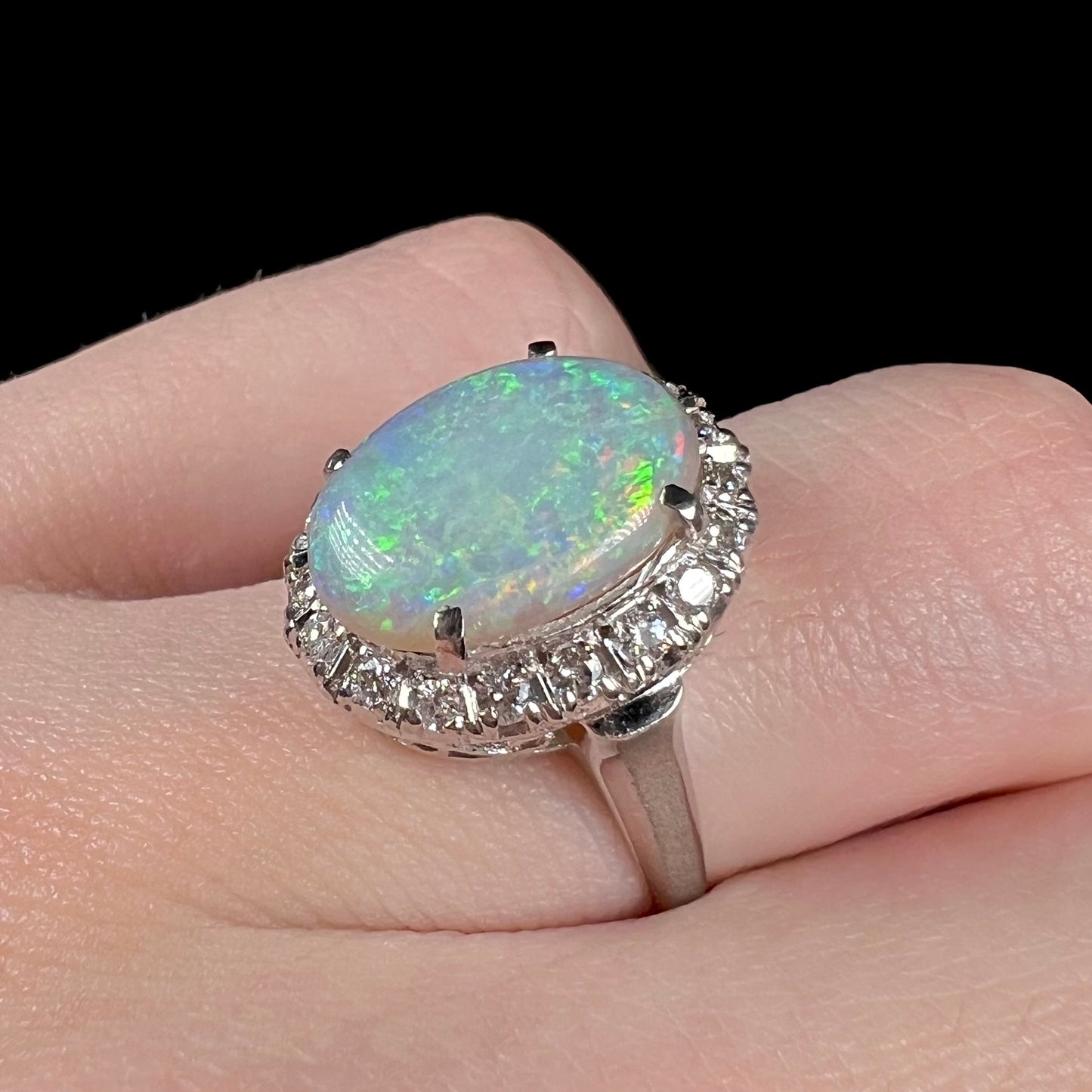 Macro view of a 1950's opal and diamond halo engagement ring on a finger.