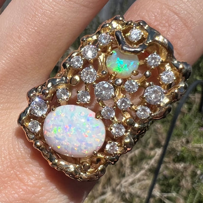 Close-up of large 1970s-style gold-tone men's opal and CZ ring, worn on finger in sunlight.