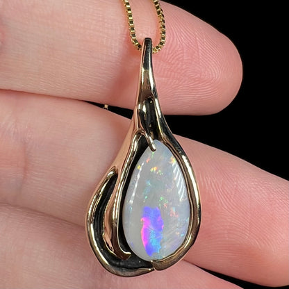 Close-up of a c.1980s era Modernist gold opal pendant with black antiquing, held on top of fingers; the opal has a purple, blue, and magenta color bar