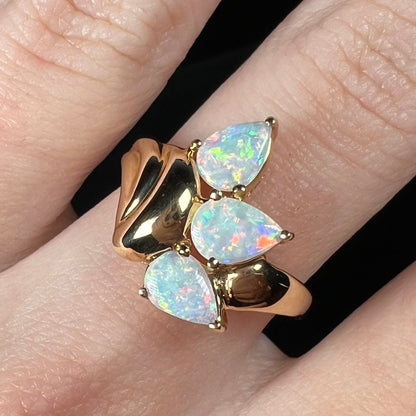 Close-up of a 1980s-style 14k gold Australian opal ring worn on a finger.  Thre ring is prong-set with three pear shaped crystal opals.
