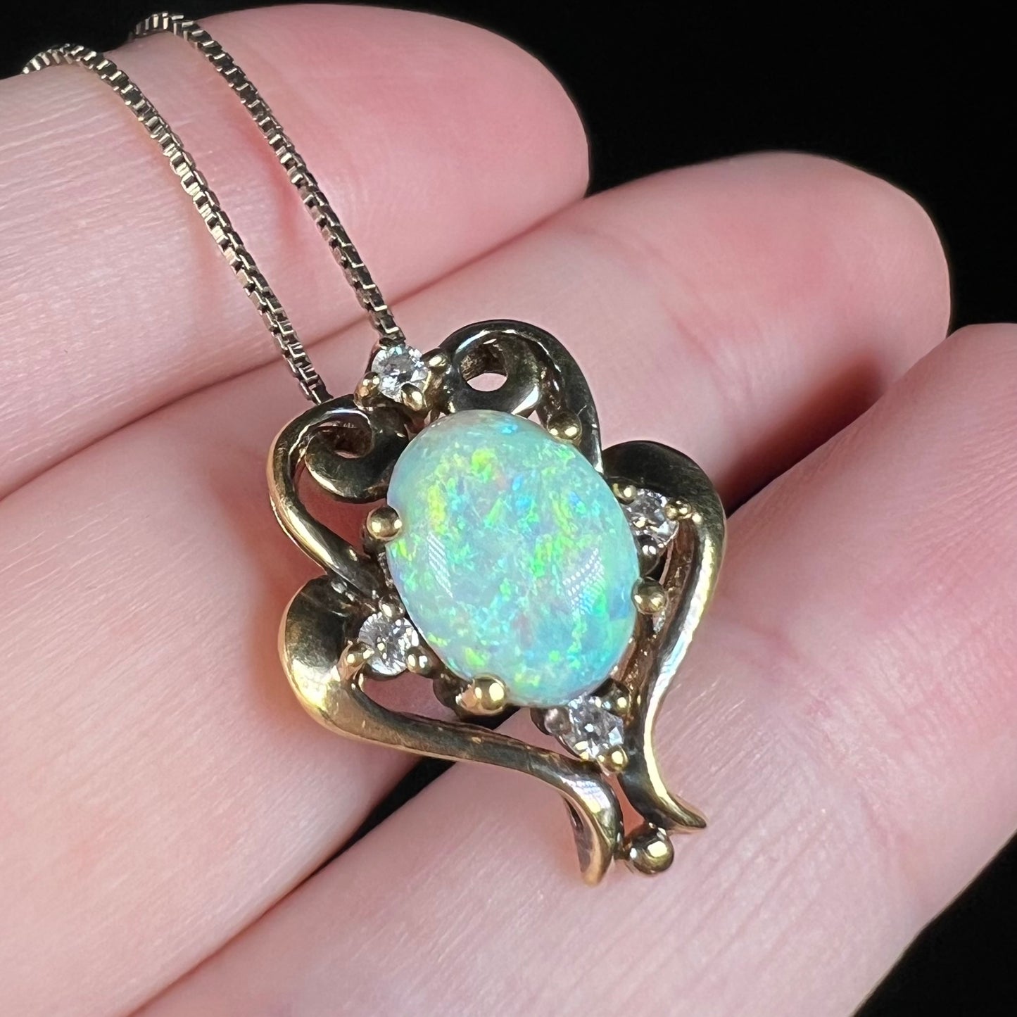 Angled close-up of a 1990s era Victorian-style lab-created opal pendant, shown on fingers.  The opal has soft green play-of-color.
