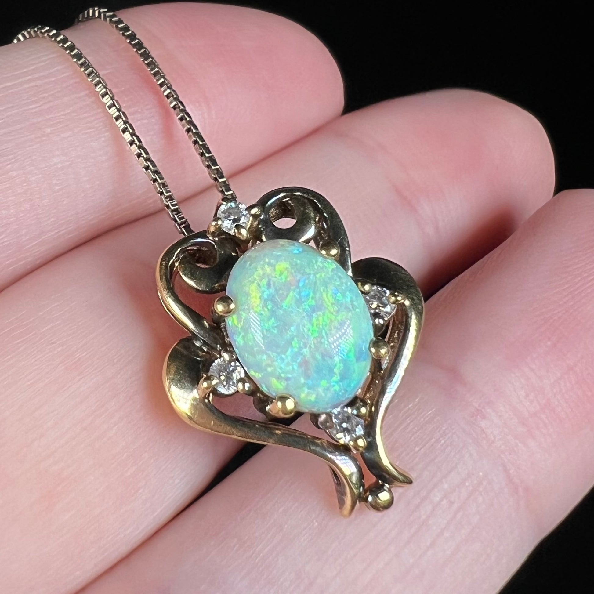 Angled close-up of a 1990s era Victorian-style lab-created opal pendant, shown on fingers.  The opal has soft green play-of-color.