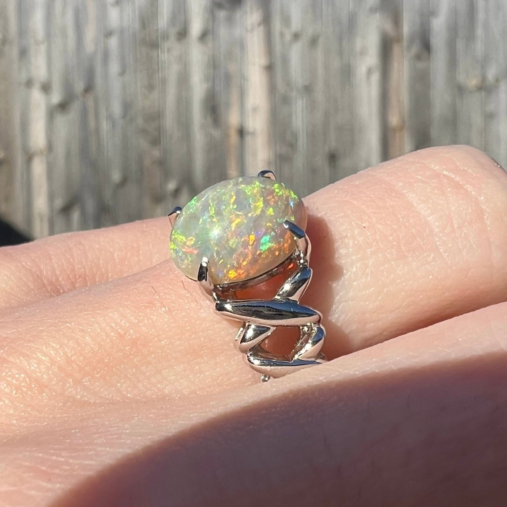 A 2.20ct opal ring showing orange fire, worn on a hand in the sunlight.