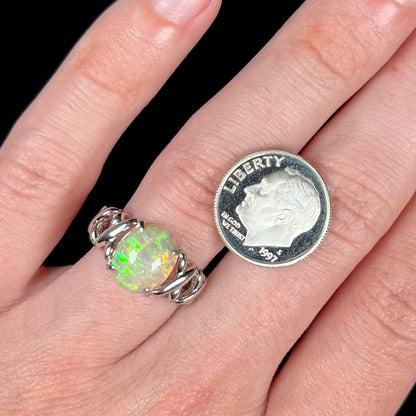 A 2.20 carat opal and platinum ring worn on a hand next to a US dime coin.