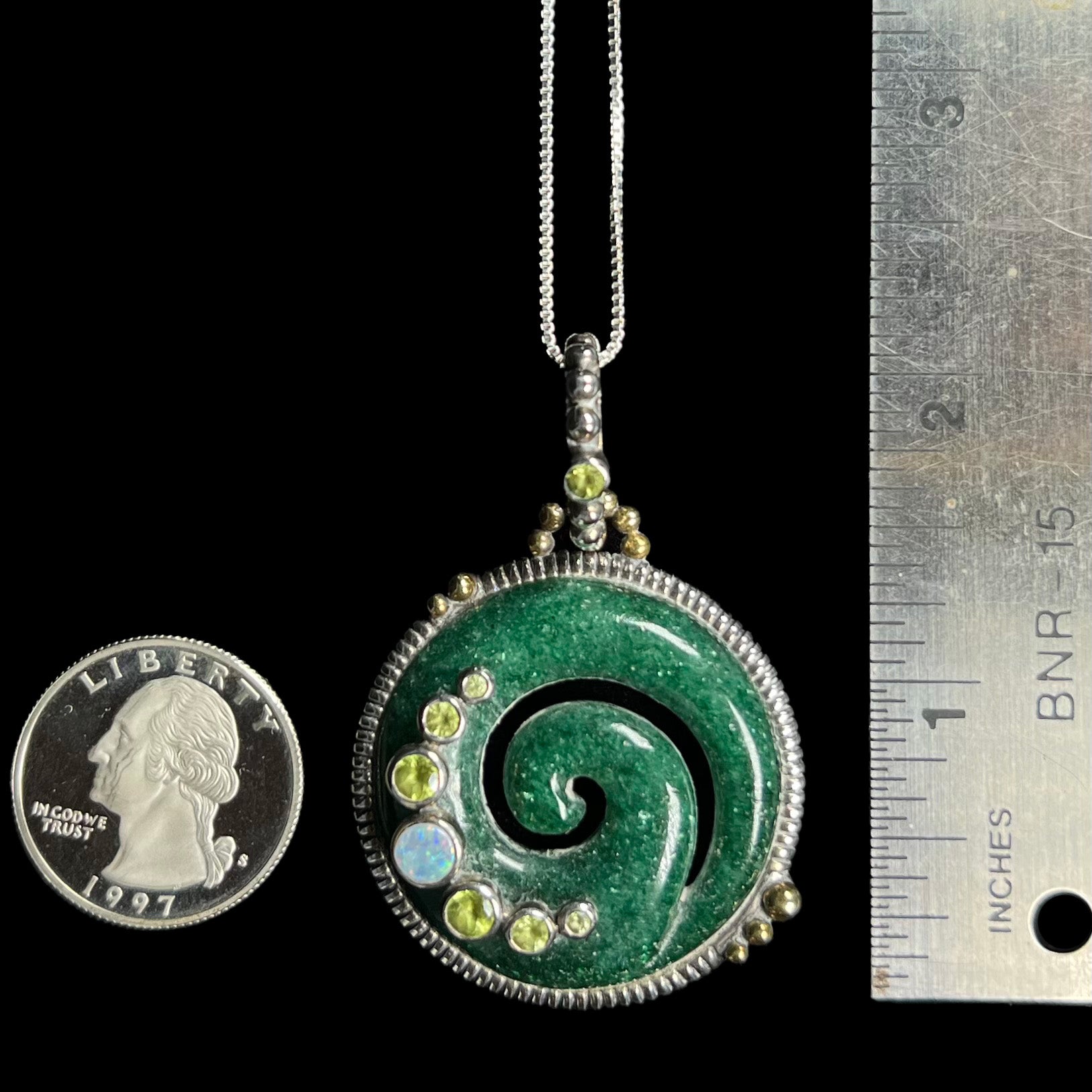 A 2.25 inch long green aventurine koru spiral pendant, shown next to a quarter coin and ruler.