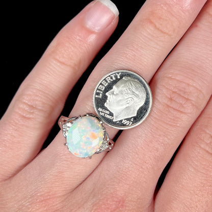 A platinum ring mounted with a 2.36ct opal worn on a finger next to a US dime coin.