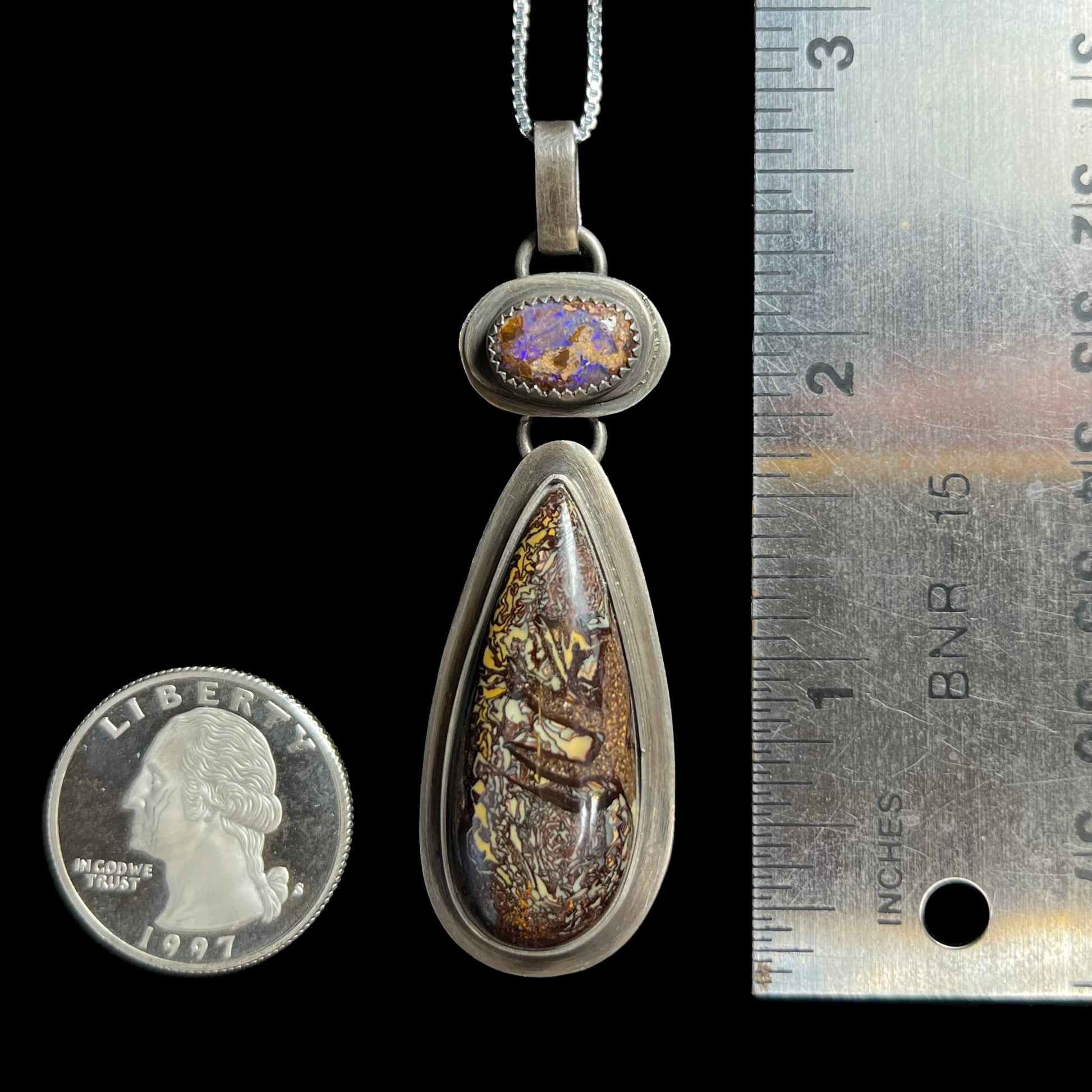2.66 inch-long pear shaped Koroit boulder opal pendant in sterling silver shown next to a ruler and US quarter coin.
