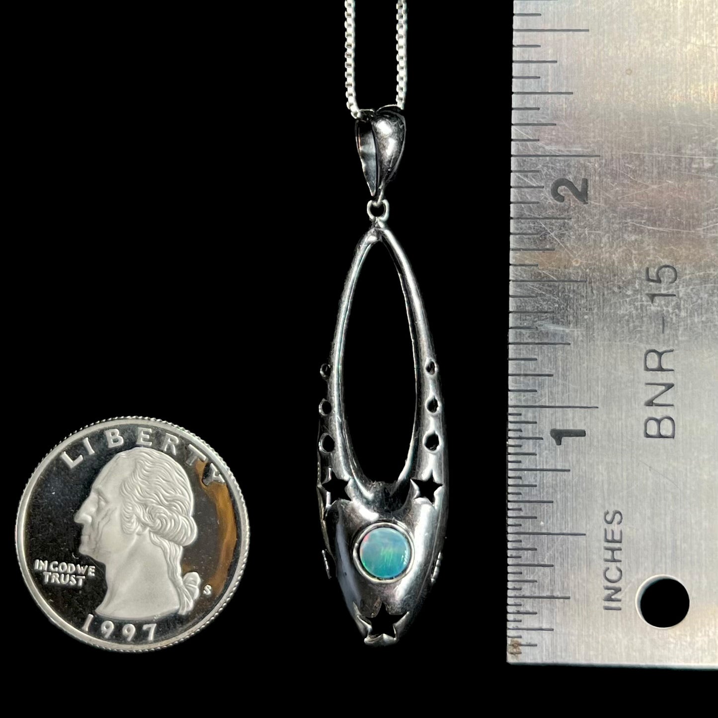 A 2 inch long sterling silver and opal ballerina shoe pendant next to a quarter coin and ruler.