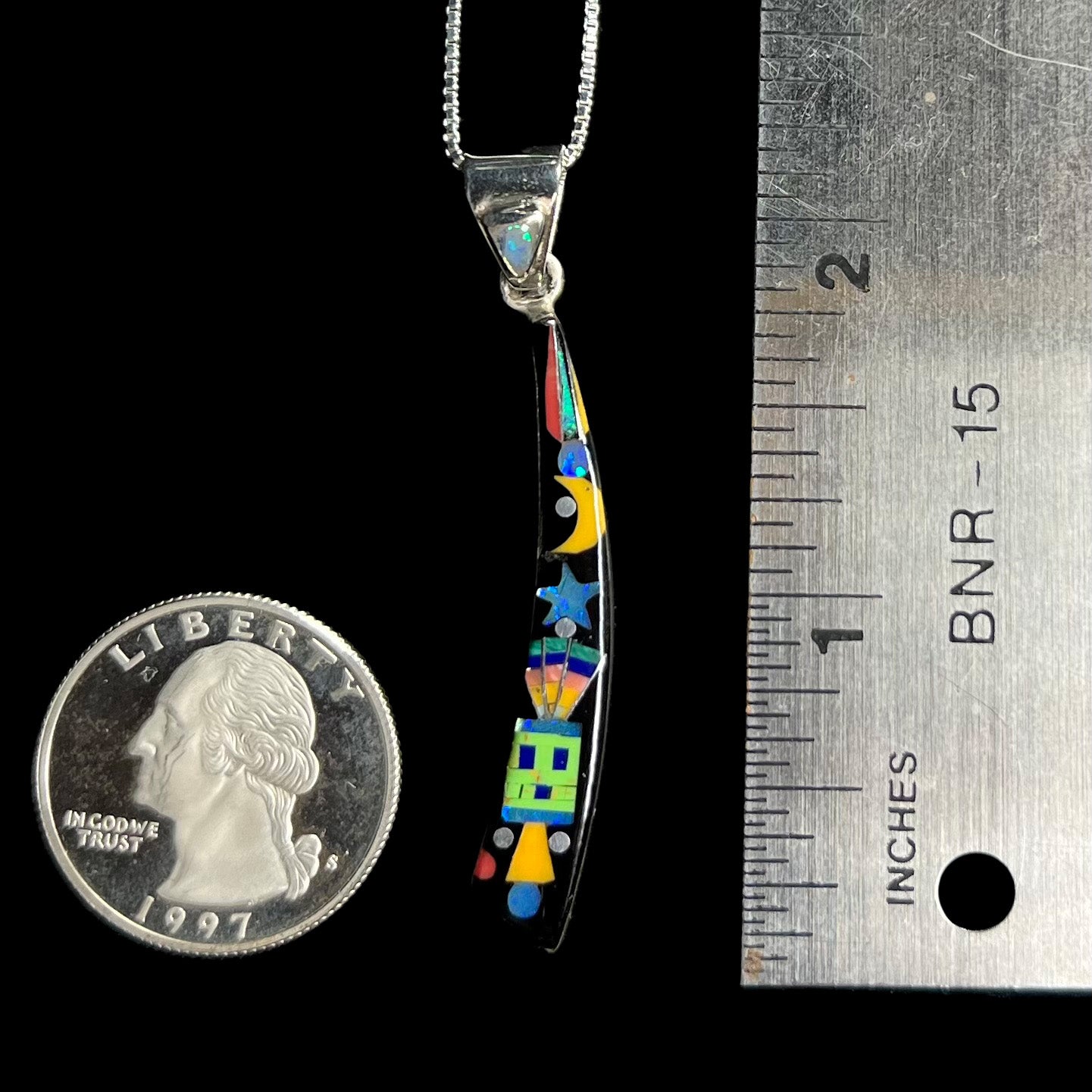 2 inch-long sterling silver opal and onyx inlay men's pendant shown on black background next to ruler and US quarter coin.