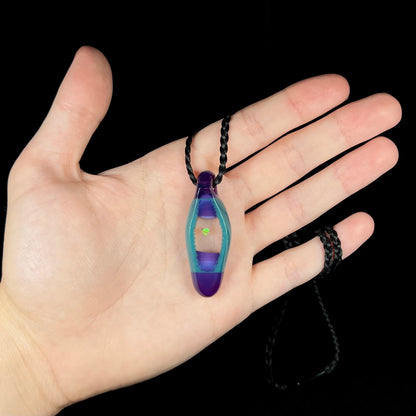 Hand holding a unisex borosilicate glass and lab-created opal necklace on a black cord, shown against a black background.