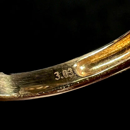 Close-up of inside of a gold ring's shank showing the engraved hallmark stamp, "3.03", indicating the center stone's carat weight.