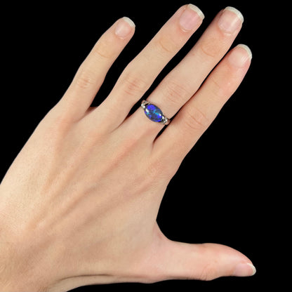 A 3.18ct black opal and diamond platinum ring worn on a hand.  The opal is set in an East-West orientation.