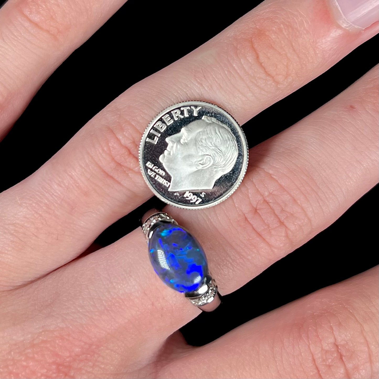 A 3.18ct black opal platinum ring worn on a hand next to a US dime coin.