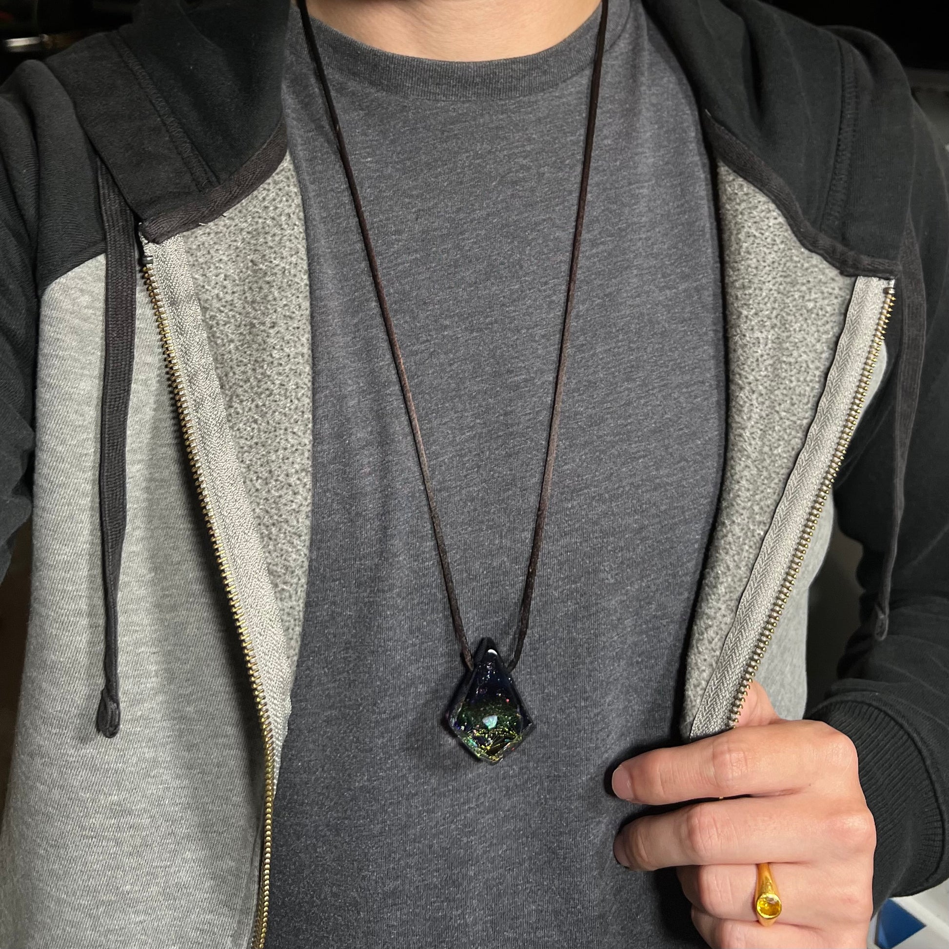A 30 inch-long opal in glass necklace on a brown cord, worn around a person's neck against a dark shirt under a hoodie.