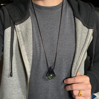 A 30 inch-long opal in glass necklace on a brown cord, worn around a person's neck against a dark shirt under a hoodie.